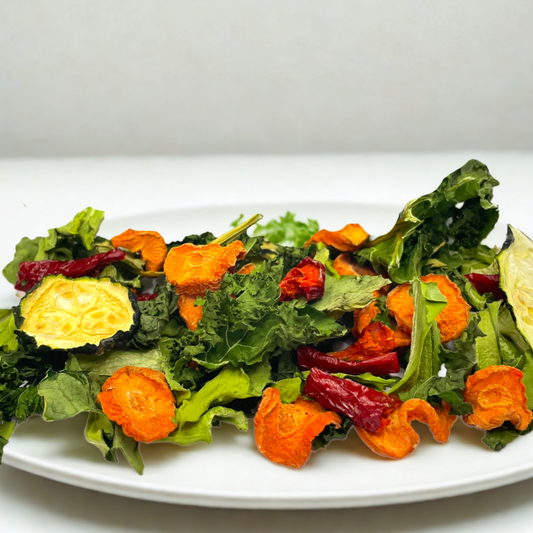 A plate of dehydrated veggie salad mix, including kale, carrot, zucchini, and capsicum, intended as a treat for small animals like rabbits and guinea pigs.
